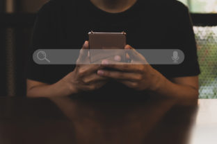 Young asian man wearing black t shirt sitting on desk hand holding smartphone to Searching for information. Using Search Console with your website.