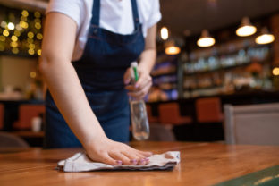 Hand of young contemporary waitress wiping wooden table with duster