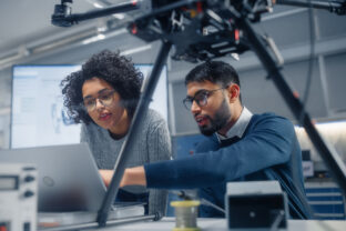 Black Male Engineer Points at Laptop Screen and Talks. Brainstorming New Drone Design With his Female Colleague. Innovative Technologies in Unmanned Aerial Vehicle Design Concept.