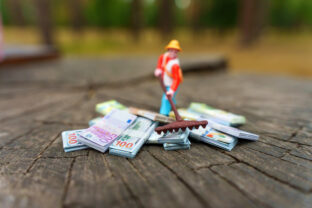 Miniature Gardener Working on Pile of Money on Wooden Surface