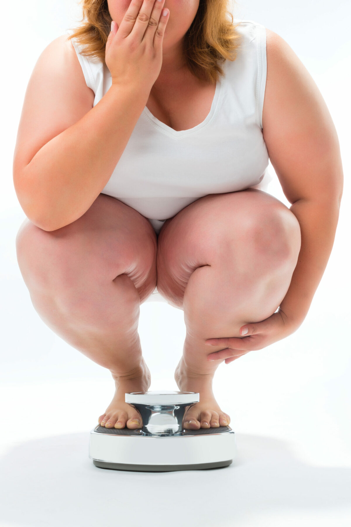 Obese young woman crouching on a scale